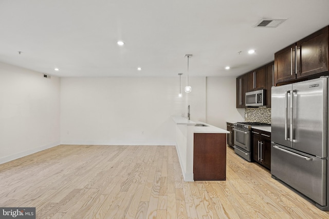 kitchen featuring sink, tasteful backsplash, decorative light fixtures, high quality appliances, and light hardwood / wood-style floors