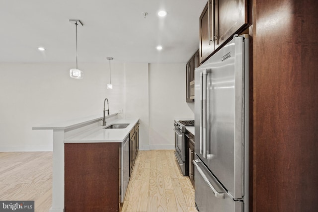 kitchen with sink, appliances with stainless steel finishes, light hardwood / wood-style floors, decorative light fixtures, and kitchen peninsula