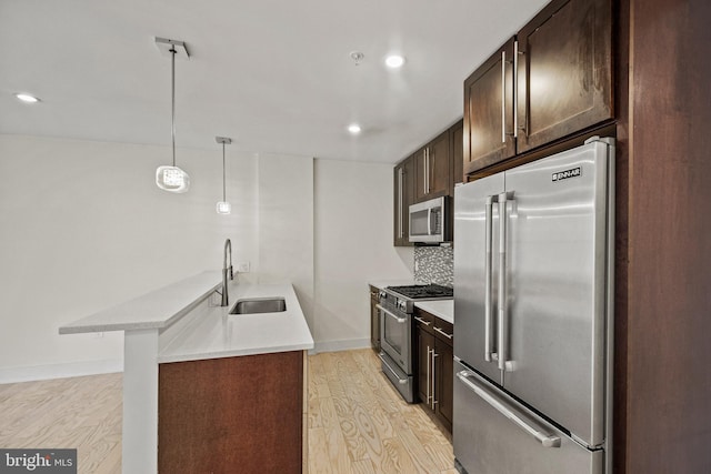 kitchen featuring pendant lighting, sink, light hardwood / wood-style floors, and high quality appliances