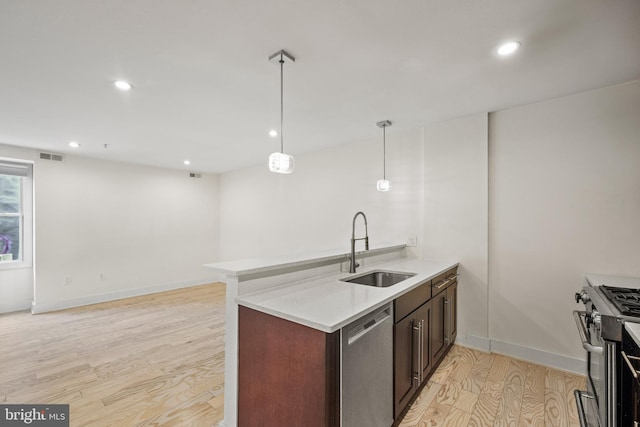 kitchen featuring sink, appliances with stainless steel finishes, hanging light fixtures, kitchen peninsula, and light wood-type flooring