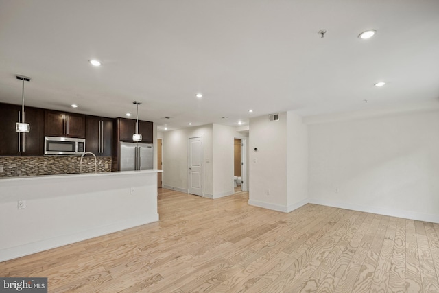 kitchen with appliances with stainless steel finishes, decorative backsplash, hanging light fixtures, dark brown cabinetry, and light wood-type flooring