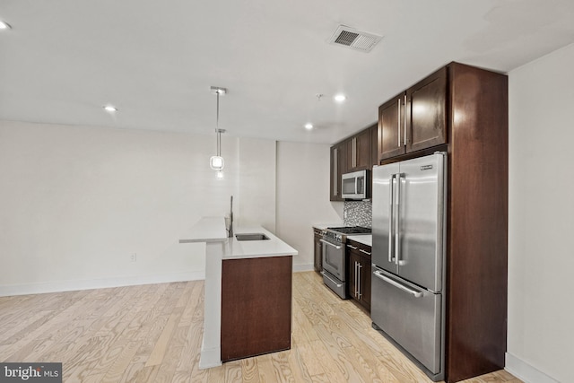 kitchen with sink, a center island with sink, high quality appliances, pendant lighting, and light hardwood / wood-style floors