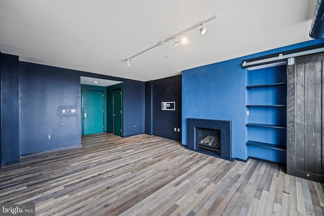 unfurnished living room featuring a fireplace, track lighting, and wood finished floors