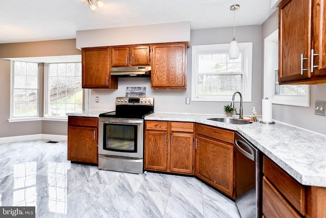 kitchen with light countertops, under cabinet range hood, a sink, appliances with stainless steel finishes, and brown cabinets