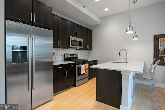 kitchen featuring sink, appliances with stainless steel finishes, tasteful backsplash, an island with sink, and decorative light fixtures