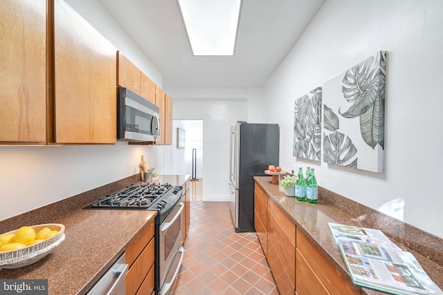 kitchen with stainless steel appliances, dark stone countertops, light tile patterned floors, and a skylight