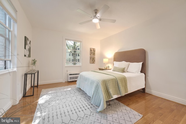 bedroom with a wall mounted air conditioner, light hardwood / wood-style flooring, and ceiling fan