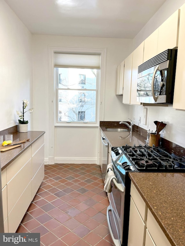 kitchen featuring sink, dark stone countertops, white cabinets, dark tile patterned flooring, and stainless steel appliances