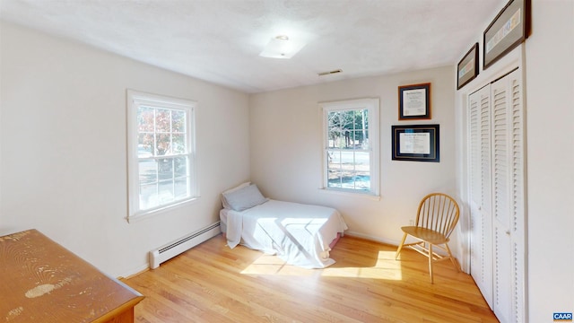 bedroom featuring a baseboard radiator, light hardwood / wood-style floors, and multiple windows