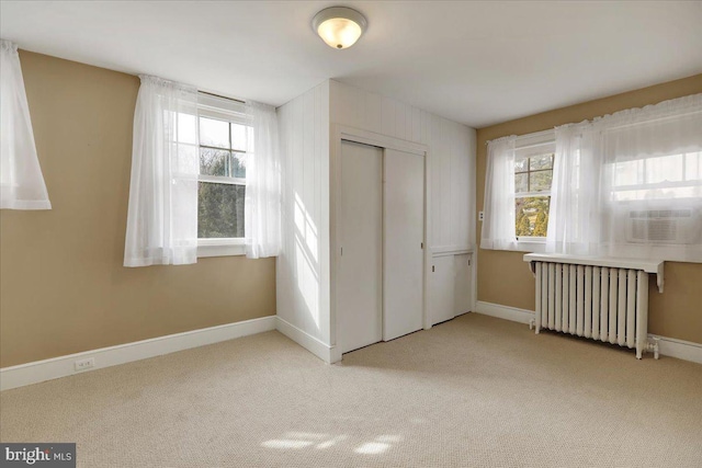 unfurnished bedroom featuring multiple windows, light carpet, radiator heating unit, and a closet