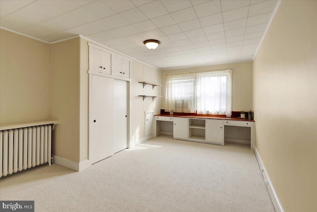 unfurnished office featuring radiator, built in desk, light colored carpet, and ornamental molding