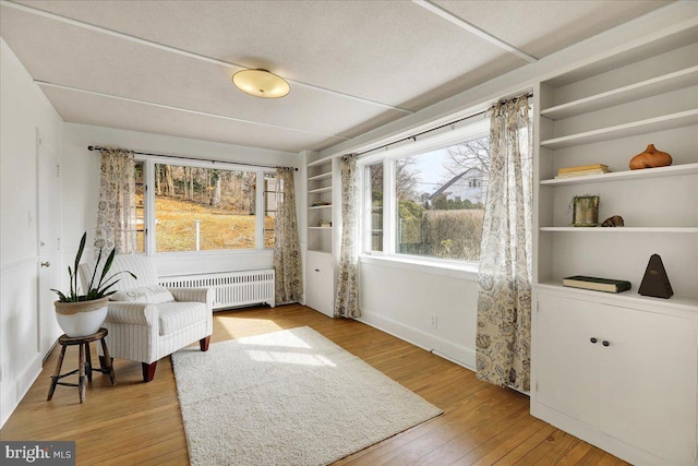 sitting room featuring built in shelves, radiator heating unit, light wood-type flooring, and plenty of natural light