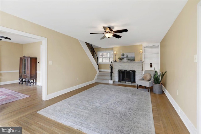 living room featuring wood-type flooring, a fireplace, and ceiling fan