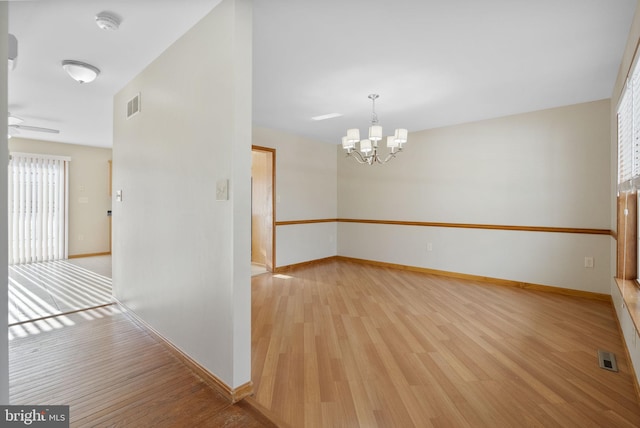 unfurnished room featuring an inviting chandelier and light wood-type flooring