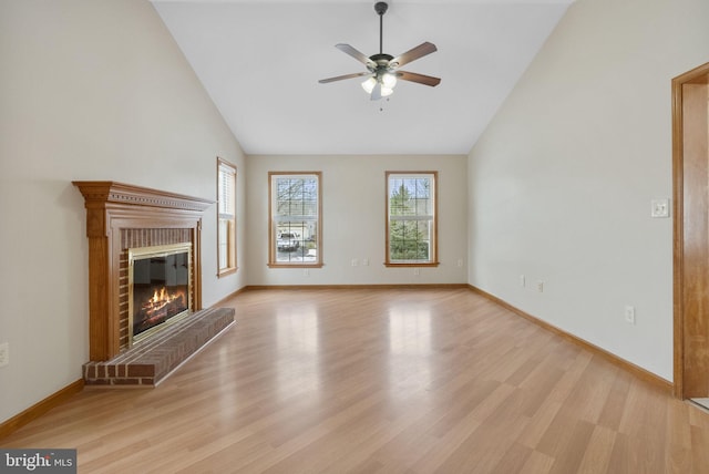 unfurnished living room with ceiling fan, vaulted ceiling, a brick fireplace, and light wood-type flooring