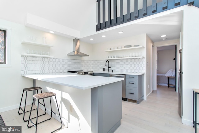 kitchen with wall chimney exhaust hood, gray cabinetry, appliances with stainless steel finishes, a kitchen breakfast bar, and kitchen peninsula