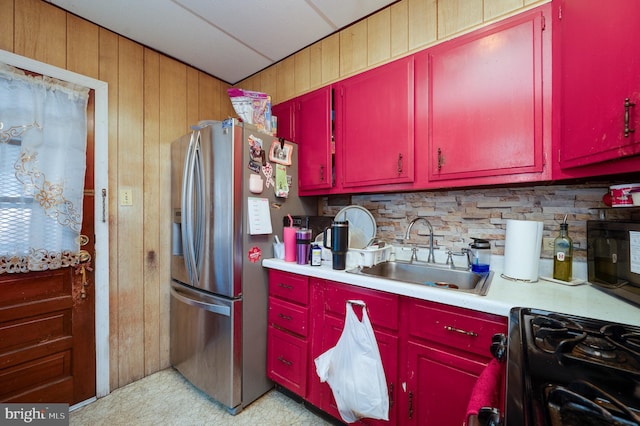 kitchen with stainless steel refrigerator with ice dispenser, gas stove, sink, wooden walls, and decorative backsplash