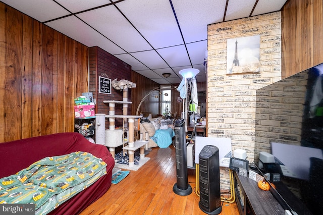 bedroom featuring a drop ceiling, wood-type flooring, brick wall, and wood walls