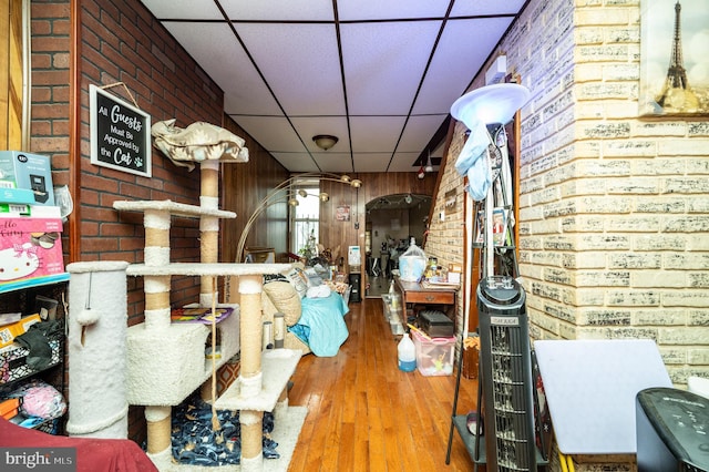 interior space featuring a drop ceiling, hardwood / wood-style flooring, and brick wall