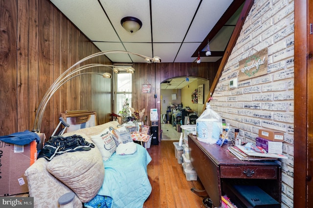 bedroom with a drop ceiling, hardwood / wood-style floors, wooden walls, and brick wall