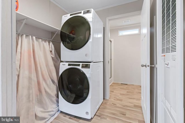 laundry room featuring stacked washing maching and dryer and light hardwood / wood-style flooring