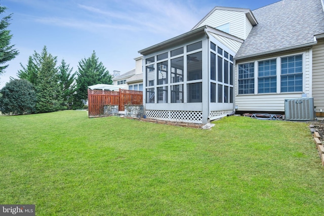 rear view of house featuring a sunroom, central AC, a yard, and roof with shingles