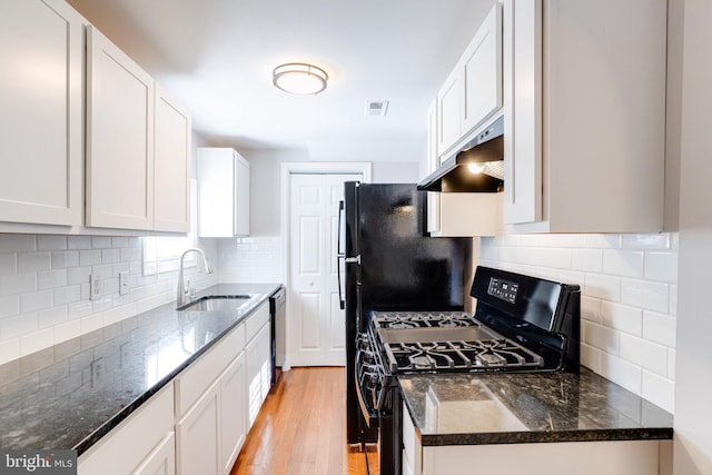 kitchen featuring gas stove, sink, white cabinets, and dark stone counters