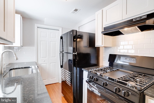 kitchen featuring sink, light hardwood / wood-style floors, black appliances, white cabinets, and dark stone counters