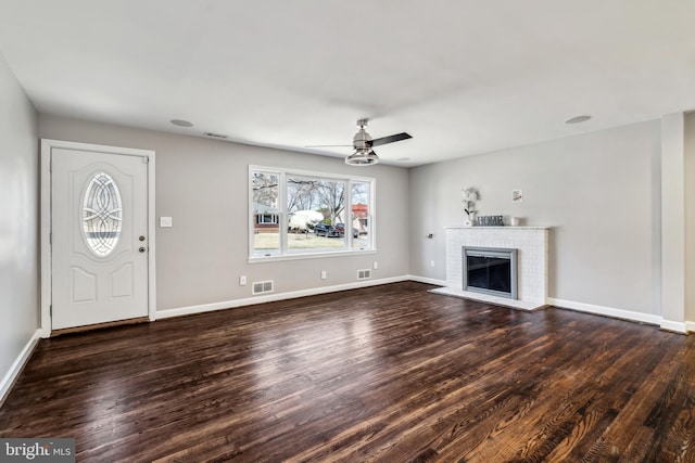 unfurnished living room featuring ceiling fan, wood finished floors, visible vents, baseboards, and a brick fireplace