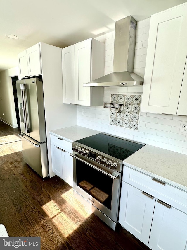 kitchen featuring wall chimney exhaust hood, light stone counters, appliances with stainless steel finishes, dark hardwood / wood-style floors, and white cabinets