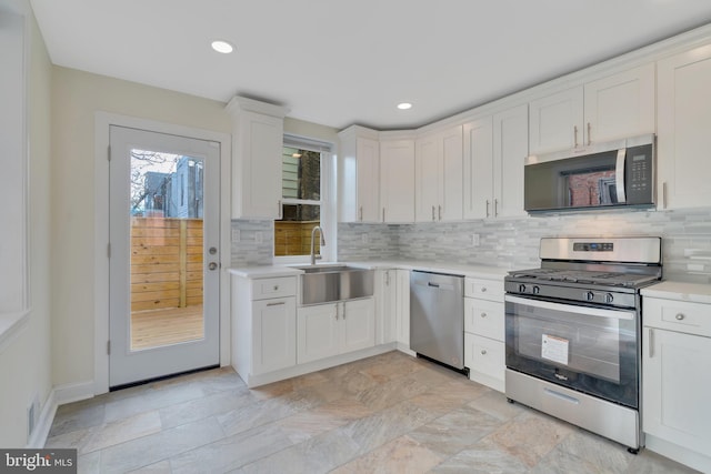 kitchen with stainless steel appliances, white cabinetry, sink, and backsplash