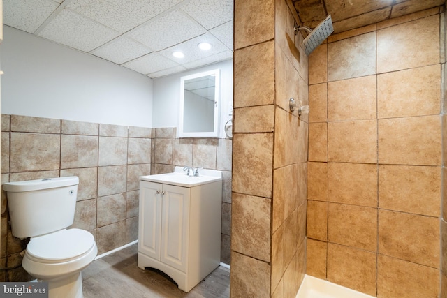 bathroom featuring walk in shower, toilet, a paneled ceiling, tile walls, and vanity