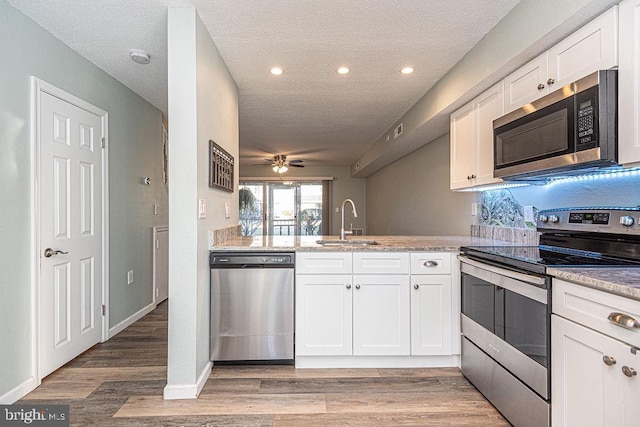 kitchen with sink, white cabinetry, stainless steel appliances, kitchen peninsula, and light wood-type flooring