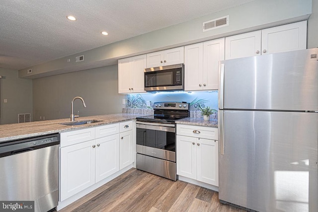 kitchen with light stone counters, stainless steel appliances, sink, and white cabinets