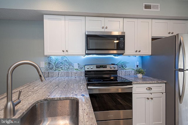 kitchen featuring white cabinetry, appliances with stainless steel finishes, sink, and light stone counters