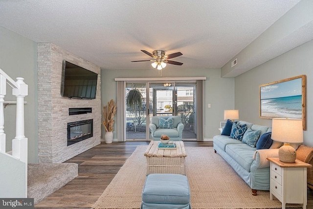 living room featuring ceiling fan, a fireplace, dark hardwood / wood-style floors, and a textured ceiling