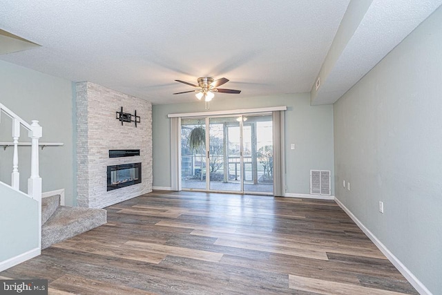 unfurnished living room featuring ceiling fan, a fireplace, dark hardwood / wood-style floors, and a textured ceiling