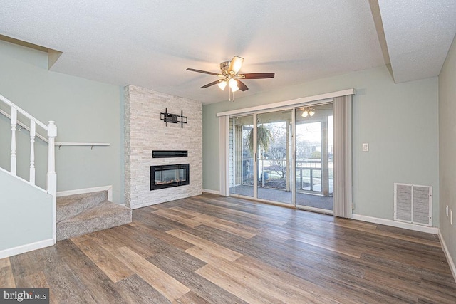 unfurnished living room featuring hardwood / wood-style flooring, ceiling fan, a stone fireplace, and a textured ceiling