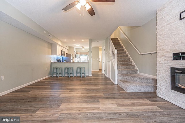 interior space featuring a stone fireplace, dark wood-type flooring, and ceiling fan