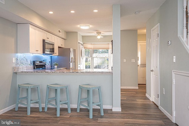 kitchen with light stone counters, a kitchen bar, white cabinets, and appliances with stainless steel finishes