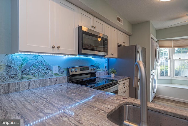 kitchen featuring white cabinetry, light stone countertops, a textured ceiling, and appliances with stainless steel finishes