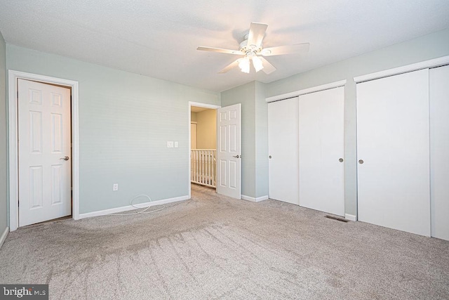 unfurnished bedroom with light carpet, ceiling fan, and multiple closets