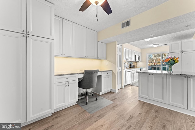 office with built in desk, sink, light wood-type flooring, ceiling fan, and a textured ceiling