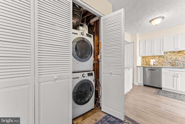 clothes washing area with sink, light hardwood / wood-style flooring, a textured ceiling, and stacked washing maching and dryer