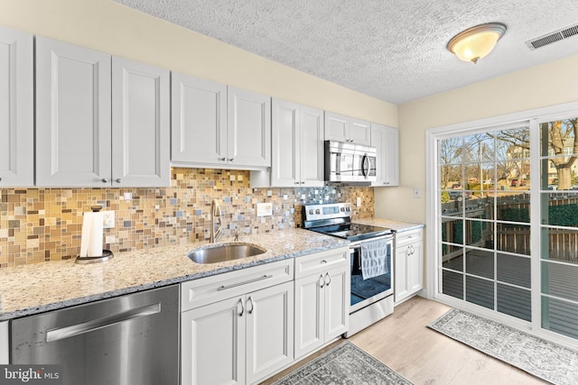 kitchen featuring sink, light hardwood / wood-style flooring, appliances with stainless steel finishes, decorative backsplash, and white cabinets