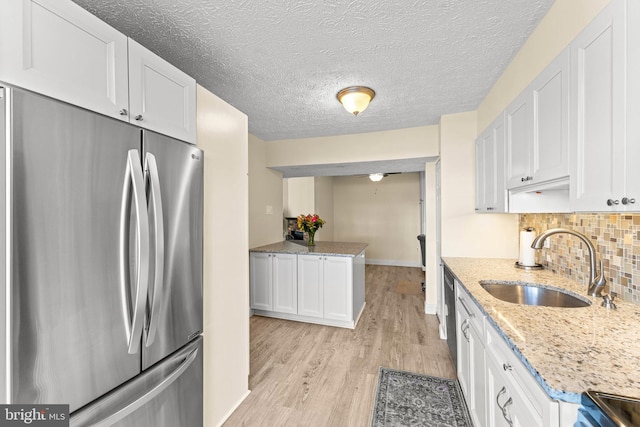 kitchen with white cabinetry, stainless steel fridge, sink, and light stone counters