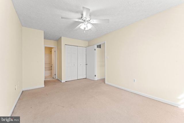 unfurnished bedroom featuring ensuite bath, light colored carpet, a textured ceiling, a closet, and ceiling fan