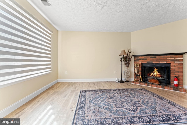 unfurnished living room with hardwood / wood-style floors, a textured ceiling, and a brick fireplace