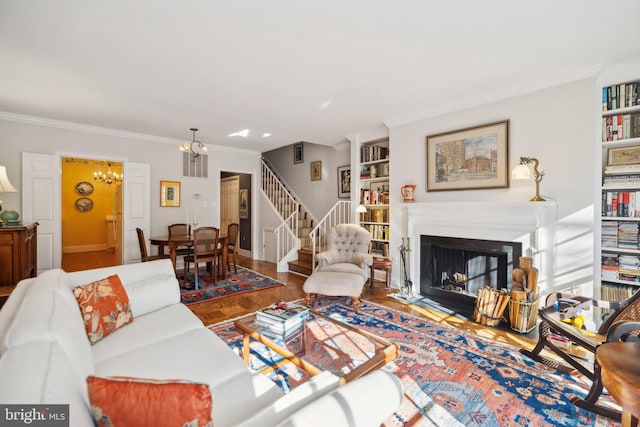 living room with ornamental molding, built in features, and an inviting chandelier