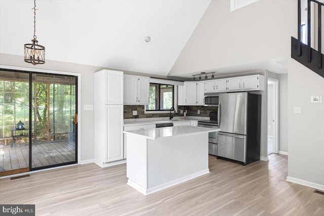 kitchen with appliances with stainless steel finishes, pendant lighting, high vaulted ceiling, tasteful backsplash, and white cabinetry